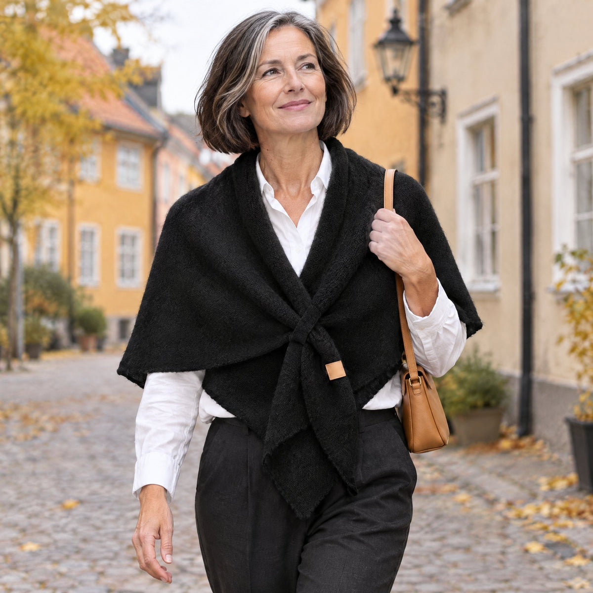 Woman walking in town wearing The Loop Shawl in black over a white shirt